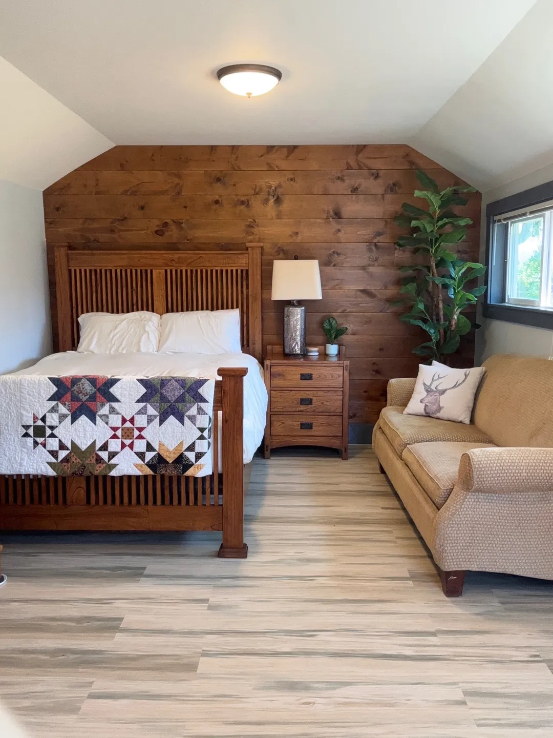 Cozy bedroom with wooden accents, a patchwork quilt, and a beige sofa by the window.